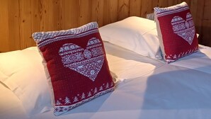 A bed with white linens and two heart-patterned pillows, a wooden headboard, and a painting of a tree on the wall. - ABRIES HOTEL  (Abriès-Ristolas)