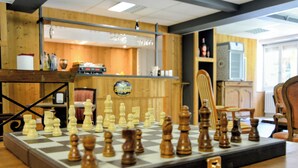 A chessboard set up on a table in a room with wooden walls and a bar area in the background. - ABRIES HOTEL  (Abriès-Ristolas)