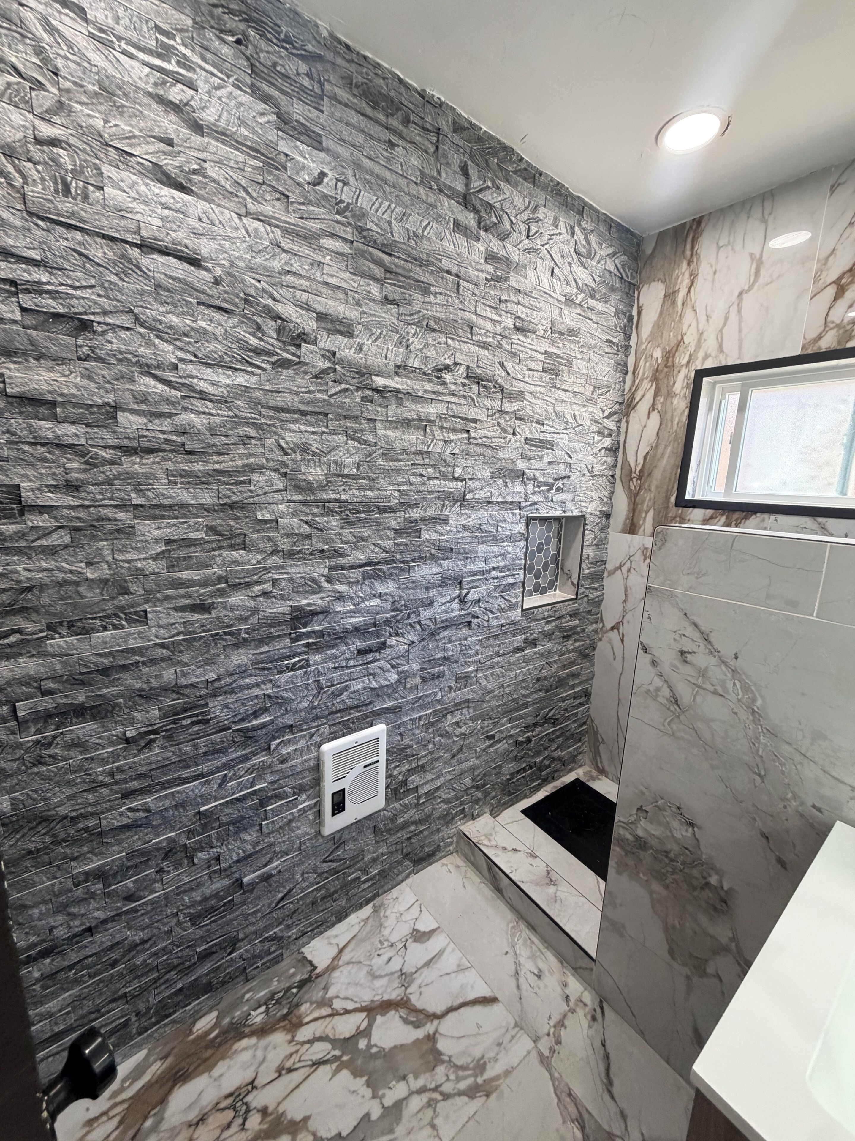 A bathroom with a stone wall, a shower area, and a marble floor.