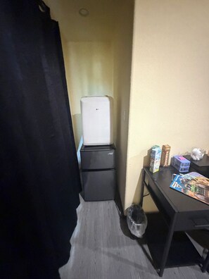 A compact room with a refrigerator, a small table with items, and a trash bin.
