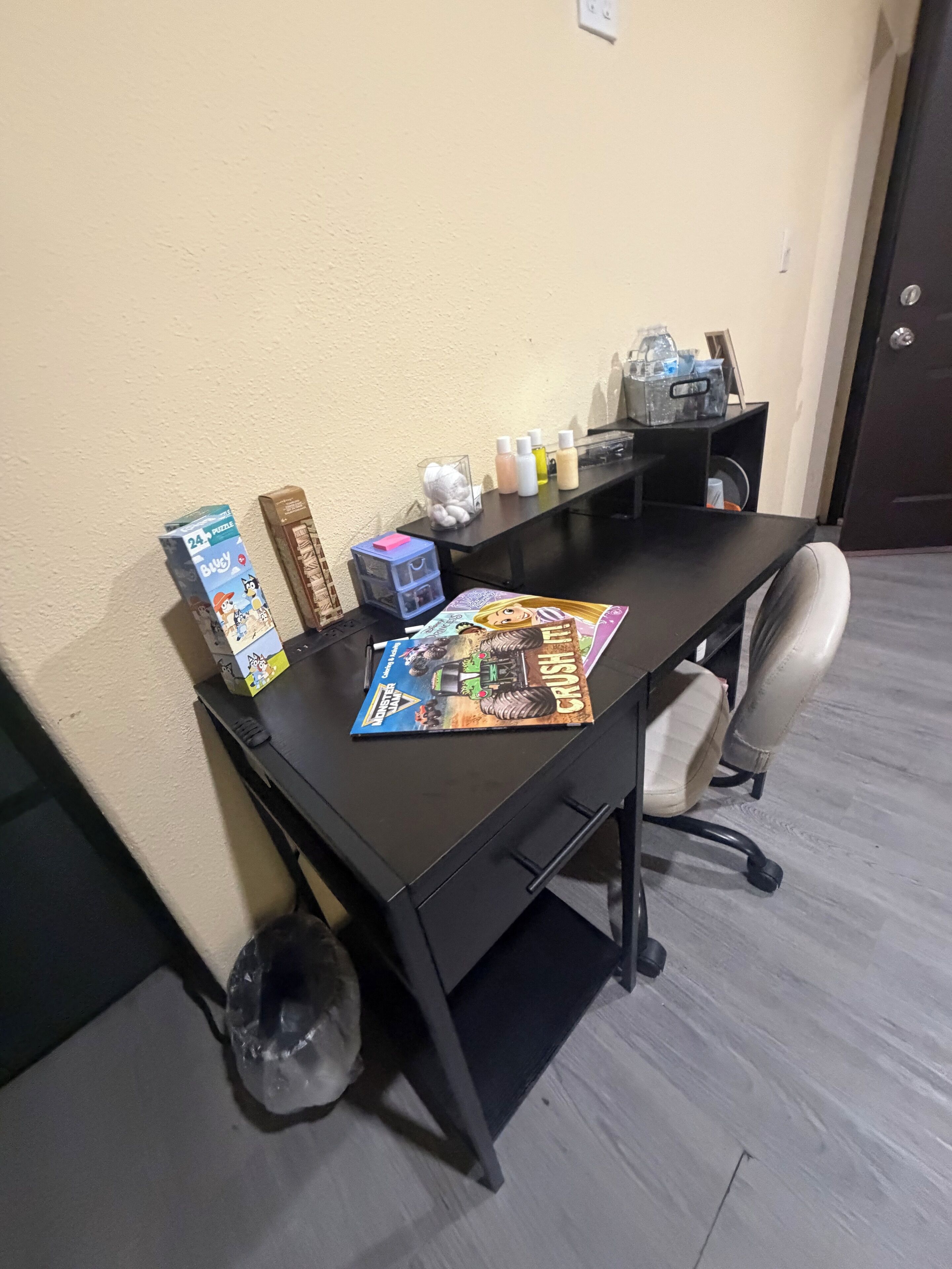A desk with a board game, a trash bin, and a water bottle.