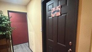 A hallway with a wooden floor, a red door, and a door with a sign.