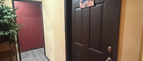 A hallway with a wooden floor, a red door, and a door with a sign.