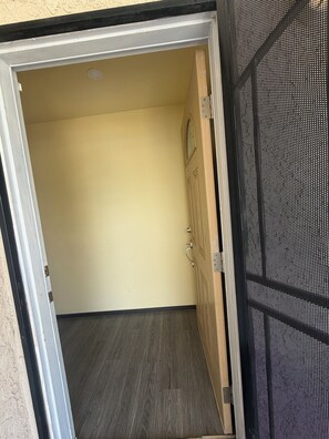 Eine geöffnete Tür, die in einen Raum führt, mit einem hölzernen Türrahmen, einer strukturierten Wand und einem dunklen Holzboden.