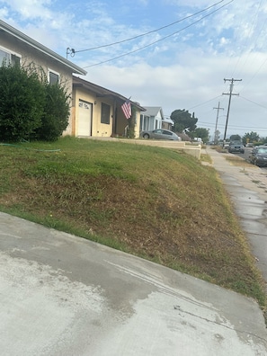 A residential street with houses, a grassy area, and parked cars.