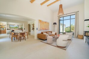 A spacious living area with a dining table, sofas, and a large window offering a view of the outdoors. - Villa Eméa |Pool, gym & pétanque court (Le Puy-Sainte-Réparade)