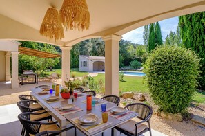 An outdoor dining area with a table set for four, surrounded by chairs, and overlooking a pool and garden. - Villa Eméa |Pool, gym & pétanque court (Le Puy-Sainte-Réparade)