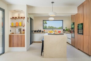 Une cuisine moderne dotée d’un îlot central, de meubles en bois et d’une grande fenêtre offrant une vue sur la verdure.