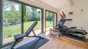 Een sportschool thuis met trainingsapparatuur, grote ramen en uitzicht op een tuin.
