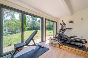 A home gym with exercise equipment, large windows, and a view of a garden. - Villa Eméa |Pool, gym & pétanque court (Le Puy-Sainte-Réparade)