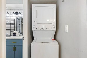 A compact laundry room with a washing machine and dryer, a sink with a mirror, and a blue cabinet with gold handles. - Modern King Condo Pool and Minutes to Old Town 208 (Scottsdale)