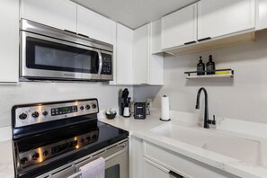 A modern kitchen with a stainless steel microwave, a black oven, a coffee maker, and a sink with a black faucet. - Modern King Condo Pool and Minutes to Old Town 208 (Scottsdale)