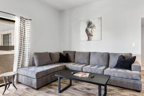 Ein modernes Wohnzimmer mit einem grauen Ecksofa, einem kleinen runden Tisch und einem Bild an der Wand.