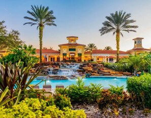 Een hotel met een zwembad, palmbomen en een waterval.