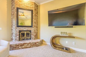 A living room with a brick fireplace, a mounted television, and a unique curved console table.