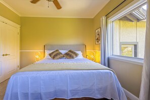 A bedroom with a bed, bedside lamps, a ceiling fan, and a window with curtains.