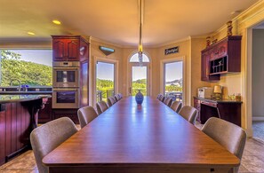 A spacious kitchen with a long dining table, built-in appliances, and large windows offering a view of the outdoors.