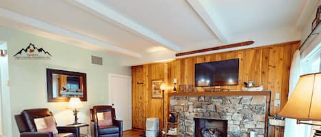 A cozy living room with a stone fireplace, leather sofas, a flat-screen TV, and a ski-themed decor.