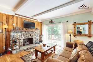 A cozy living room with a stone fireplace, wooden walls, a flat-screen TV, and a comfortable sofa. - Bee Branch 3 - Walk to the Ski Slopes (Sugar Mountain)