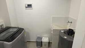 Et lille badeværelse med vaskemaskine, toilet, håndvask og varmtvandsbeholder.