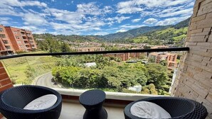 En balkon med fletningsmøbler og udsigt over by og bjerge.