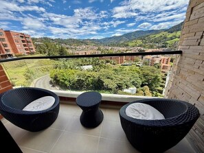 Ein Balkon mit Korbmöbeln und Blick auf Stadt und Berge.