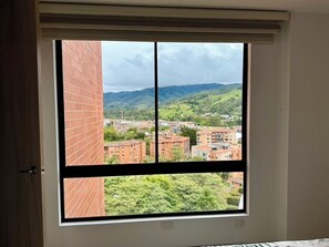 A room with a large window offering a view of a cityscape and greenery. - El Retiro apartment – peaceful, quiet, yet close to downtown with LOVELY views! (Retiro)