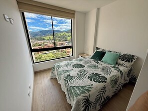 A bedroom with a bed, a window, and a view of a landscape. - El Retiro apartment – peaceful, quiet, yet close to downtown with LOVELY views! (Retiro)