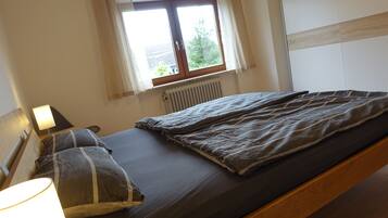 Ein Einzelbett mit Kopfstütze, eine Nachttischlampe und ein Fenster mit Vorhängen.