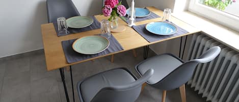 Een eettafel met twee stoelen, een vaas met bloemen en een raam met uitzicht op groen.