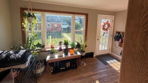 A room with a large window, a wooden floor, a bench, and various potted plants. - Little League Getaway - Sleeps 10 - Spacious 4-bedroom, mins from stadium (Williamsport)
