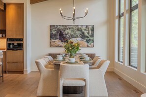 A dining area with a round table, six chairs, and a chandelier. - Ultra-Luxury Estate w/ Nordic Spa & Concierge (Canmore)