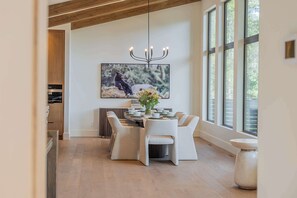 A dining area with a table set for six, a chandelier, and a large window with a view of trees. - Ultra-Luxury Estate w/ Nordic Spa & Concierge (Canmore)