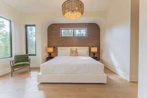 A bedroom with a large bed, two bedside lamps, a window, and a chair. - Ultra-Luxury Estate w/ Nordic Spa & Concierge (Canmore)