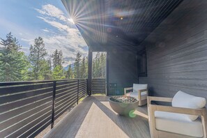 A balcony with a fire pit, seating, and a view of trees and mountains. - Ultra-Luxury Estate w/ Nordic Spa & Concierge (Canmore)