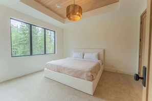 A bedroom with a large window, a bed, and a ceiling light fixture. - Ultra-Luxury Estate w/ Nordic Spa & Concierge (Canmore)