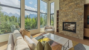 Una sala de estar moderna con ventanas amplias, una chimenea de piedra y vistas a montañas.