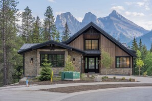A two-story mountain cabin with stone and wood exterior, large windows, and a view of the mountains. - Ultra-Luxury Estate w/ Nordic Spa & Concierge (Canmore)