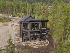 A modern two-story house with a balcony, surrounded by a forested area. - Ultra-Luxury Estate w/ Nordic Spa & Concierge (Canmore)