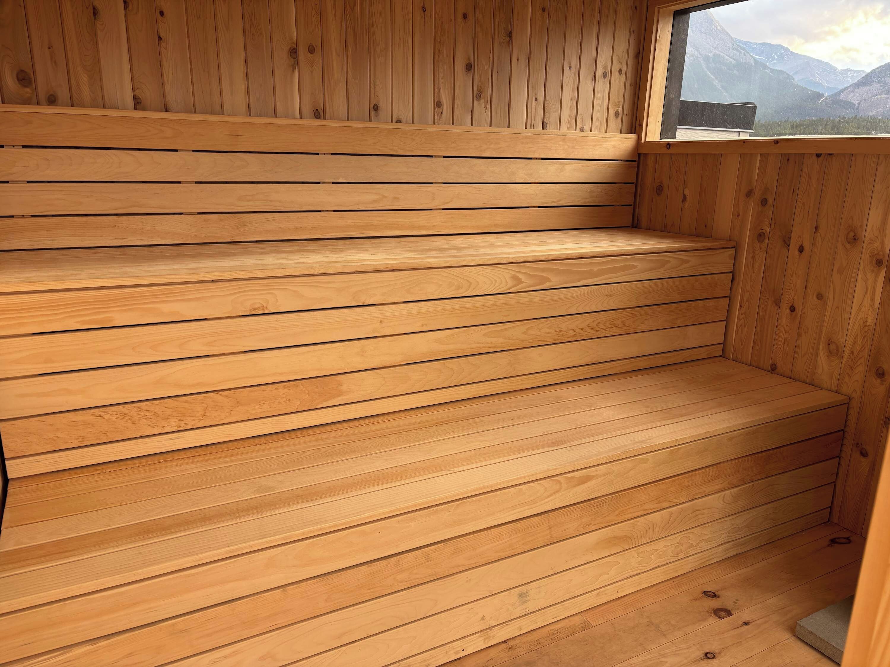 A wooden sauna with horizontal slats and a window providing a view of mountains.