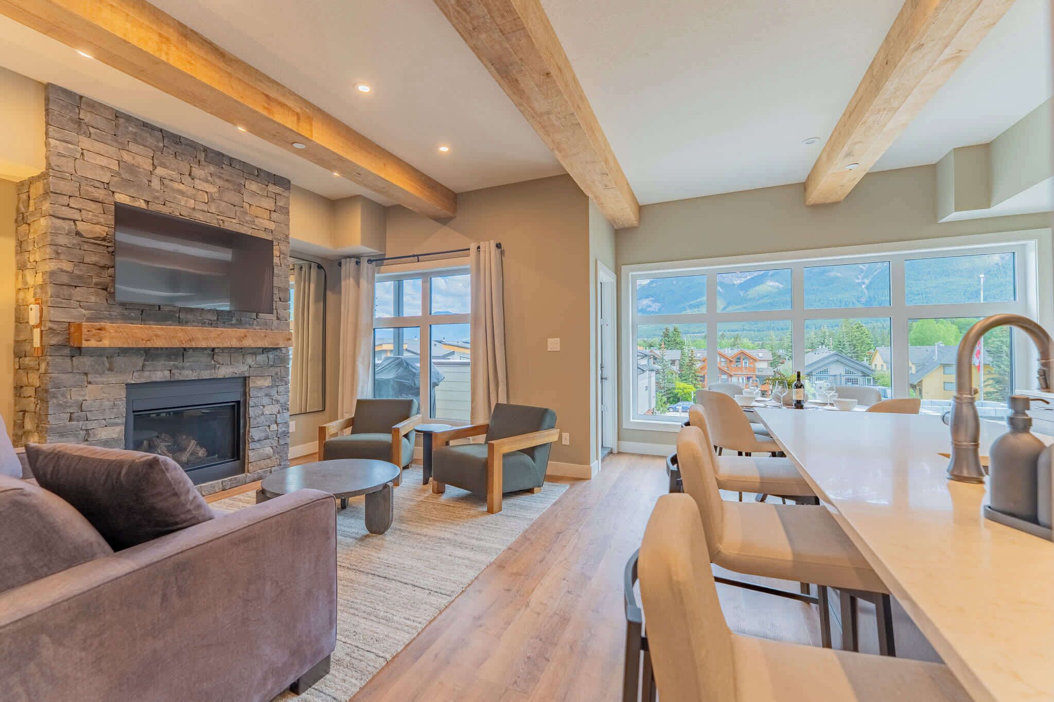 A modern living room with a stone fireplace, comfortable seating, and a view of a mountain landscape through large windows.