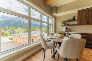 A dining area with a mountain view, wooden flooring, and a modern kitchen with dark cabinets. - Summit Suite on Main Street | Top-Floor Views (Canmore)