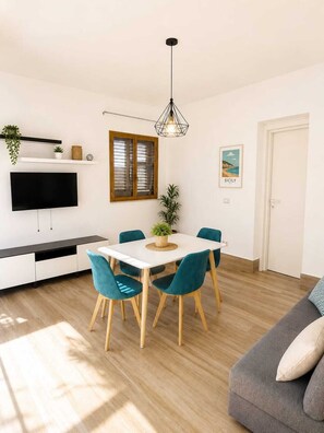 Ett modernt vardagsrum med en matplats, en platt-TV som är monterad på ett skåp, en taklampa och en dörr.