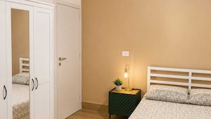 Ein Schlafzimmer mit einem Bett, einem Kleiderschrank, einem Nachttisch mit Lampe und einer Pendelleuchte.