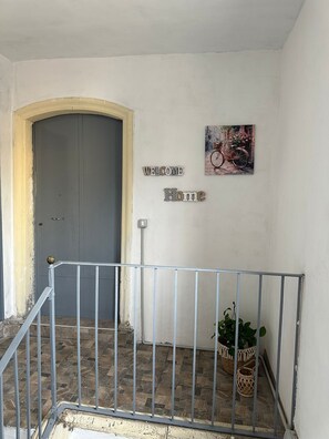 Um corredor com uma porta cinza, um letreiro de boas-vindas e uma pintura de uma bicicleta.