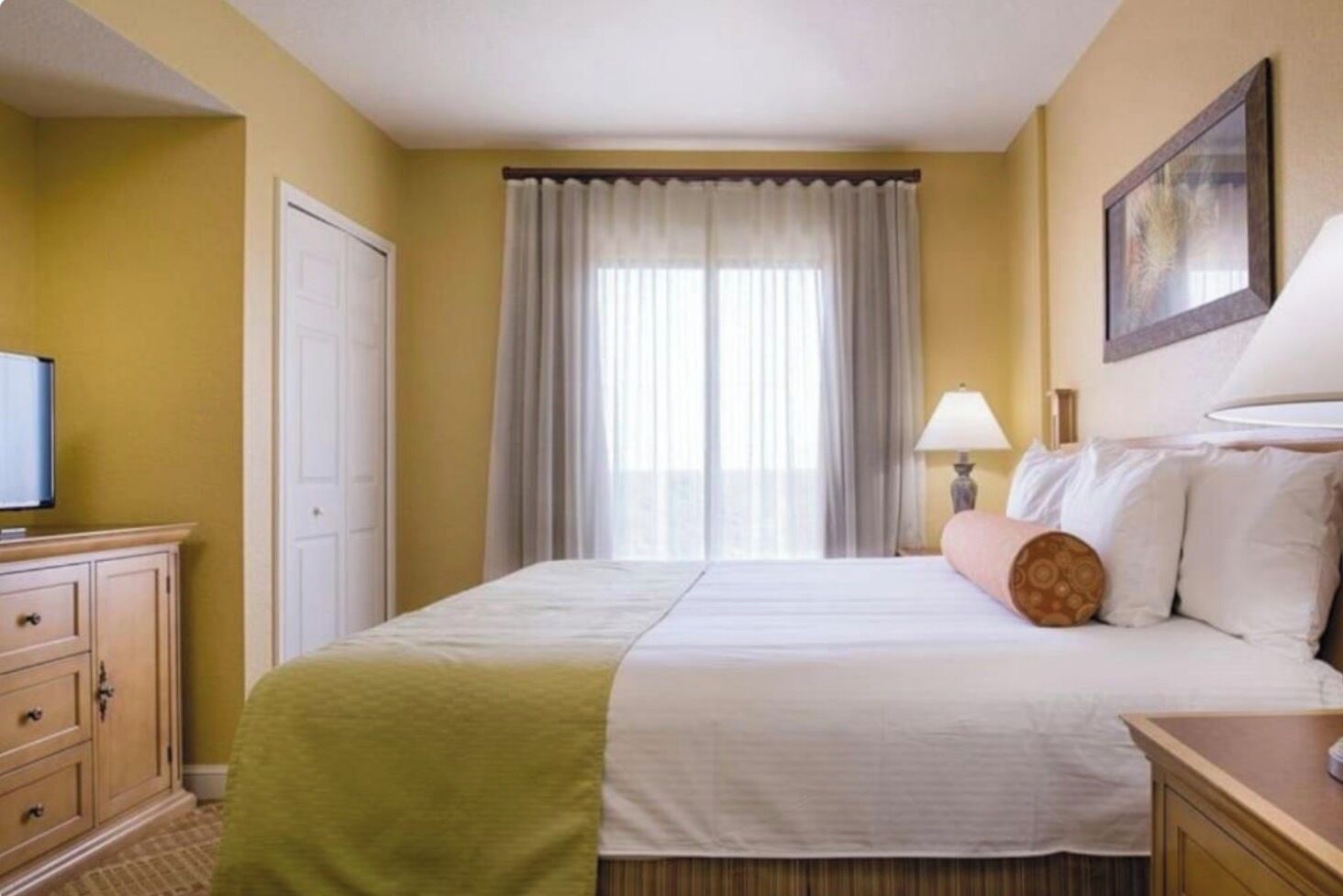 Una camera d'albergo con un letto, una televisione, una scrivania e una finestra con tende.