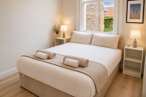 Une chambre d’hôtel avec un grand lit, deux tables de chevet, une fenêtre donnant sur un mur de briques et de la verdure, et un tableau encadré accroché au mur.