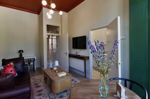 A living room with a sofa, coffee table, and a vase of flowers. There is a television mounted on the wall and a door leading to another room. - Notting Hill's Iconic Pink House Mid / Long term (London)