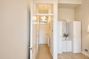 Un couloir avec une porte blanche, un miroir, une petite plante et une lampe.