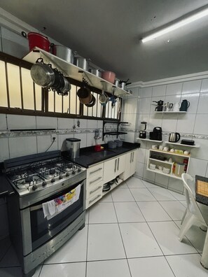 A kitchen with a gas stove, oven, and various pots and pans hanging above. - Refugio Raizes Hostel (Salvador)